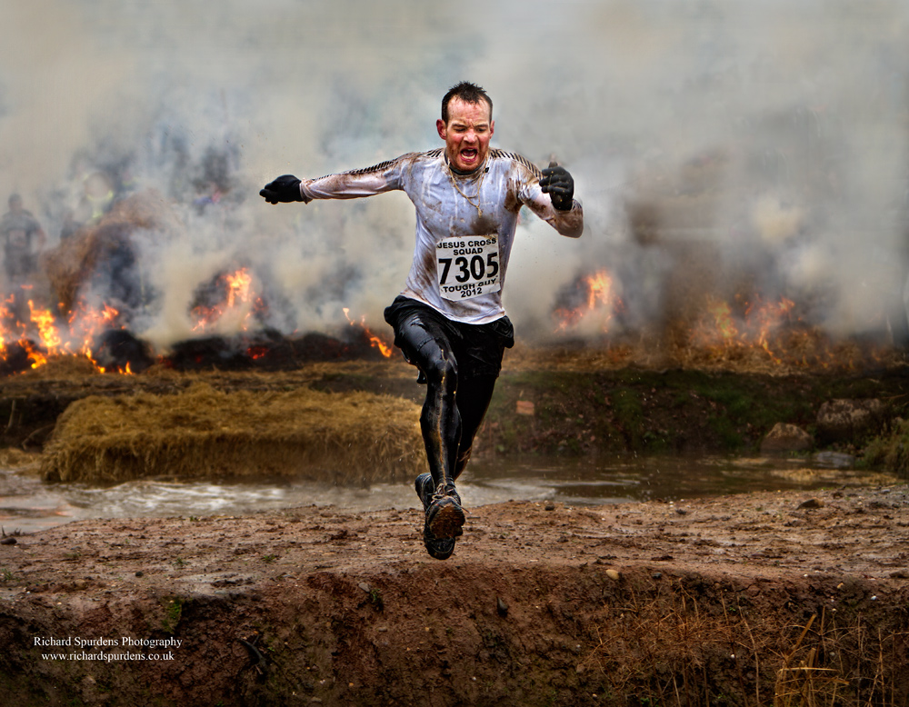 Sports Photography - Sports Photographer - a tough guy competitior runing across the water trap with lots of smoke in the background