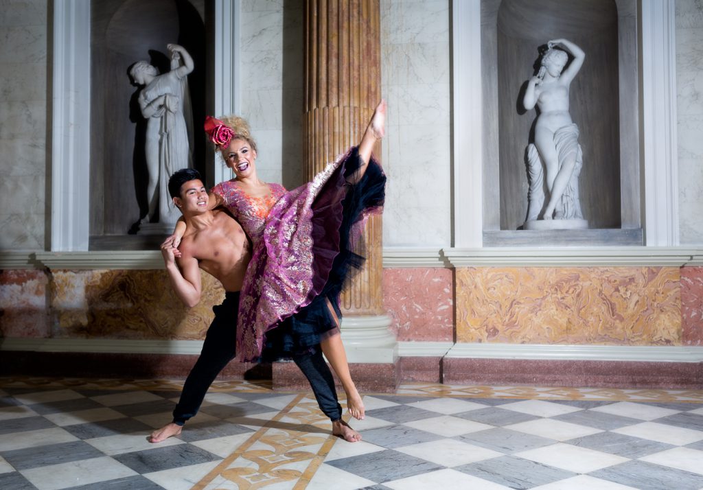 dance photographer - dance photography - colour image of two dancers one male one female the male is performing a side lift of the female as she kicks her top leg into the air. in the background are two roman statues