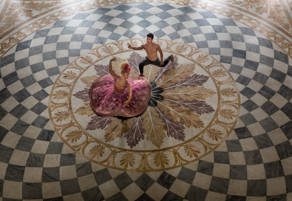 dance photographer - dance photography - two dancers one male one female in the center of a large tiled dance floor the female is performing a spin so her skirt is spinning out and the male is holding out a hand as if he was spinning her as a top