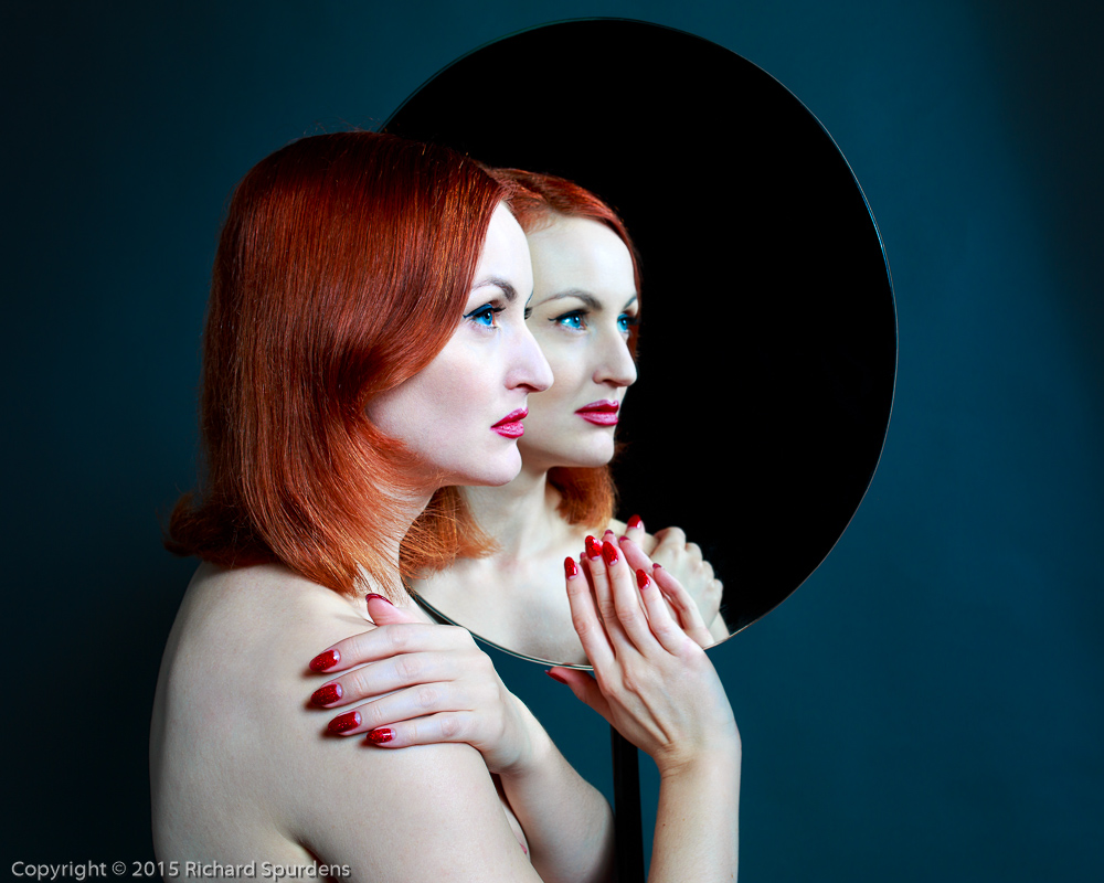 Portrait Photography - Portrait Photographer - colour image of the model reflected in a the mirror with her red nails and hair shining brightly