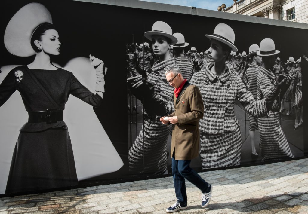 travel photography - travel photograher - images from a visit to photo london this one in colour capturing a man walking past fashion poster shot on the wall. he is engaged with reading his ticket