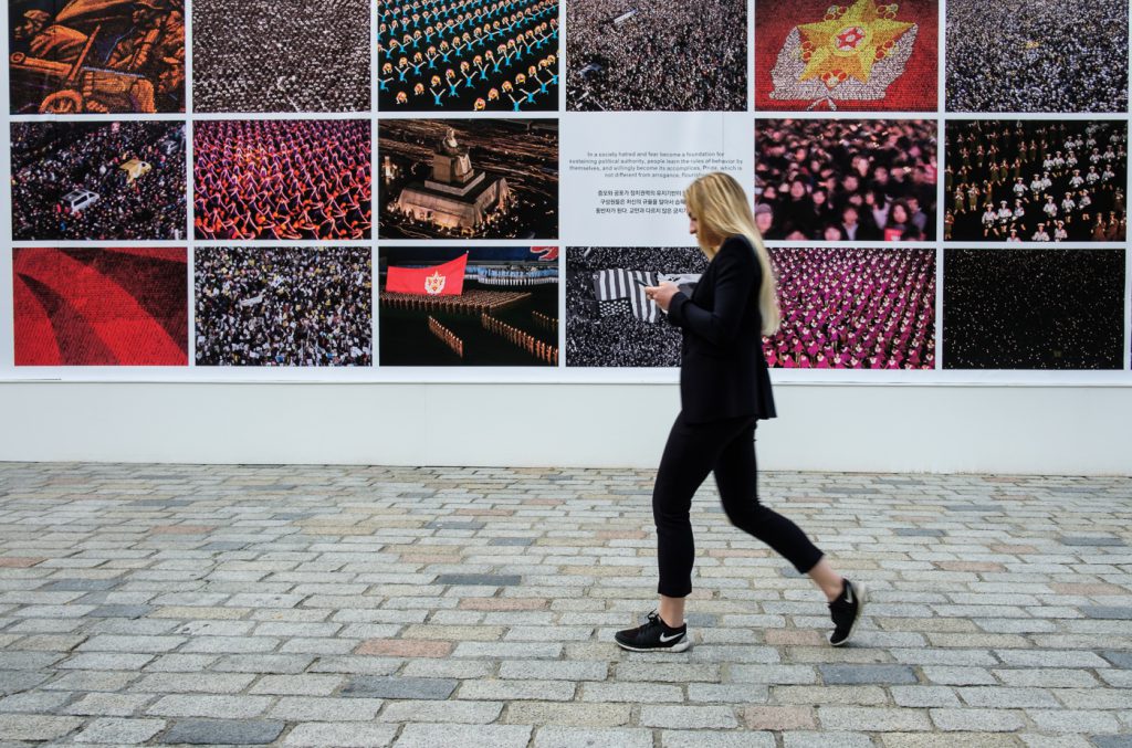 travel photography - travel photograher - images from a visit to photo london this one in colour capturing a lady looking at her phone as she strides past the dual reality wall imagess
