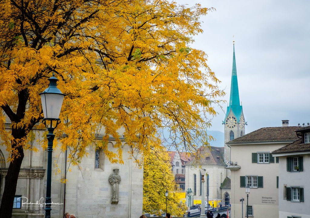 travel photography - travel photograher - images from a visit to zurich this featuring the vibrant autume colours of the trees contrasting with the blue spire of the church and off white buildings