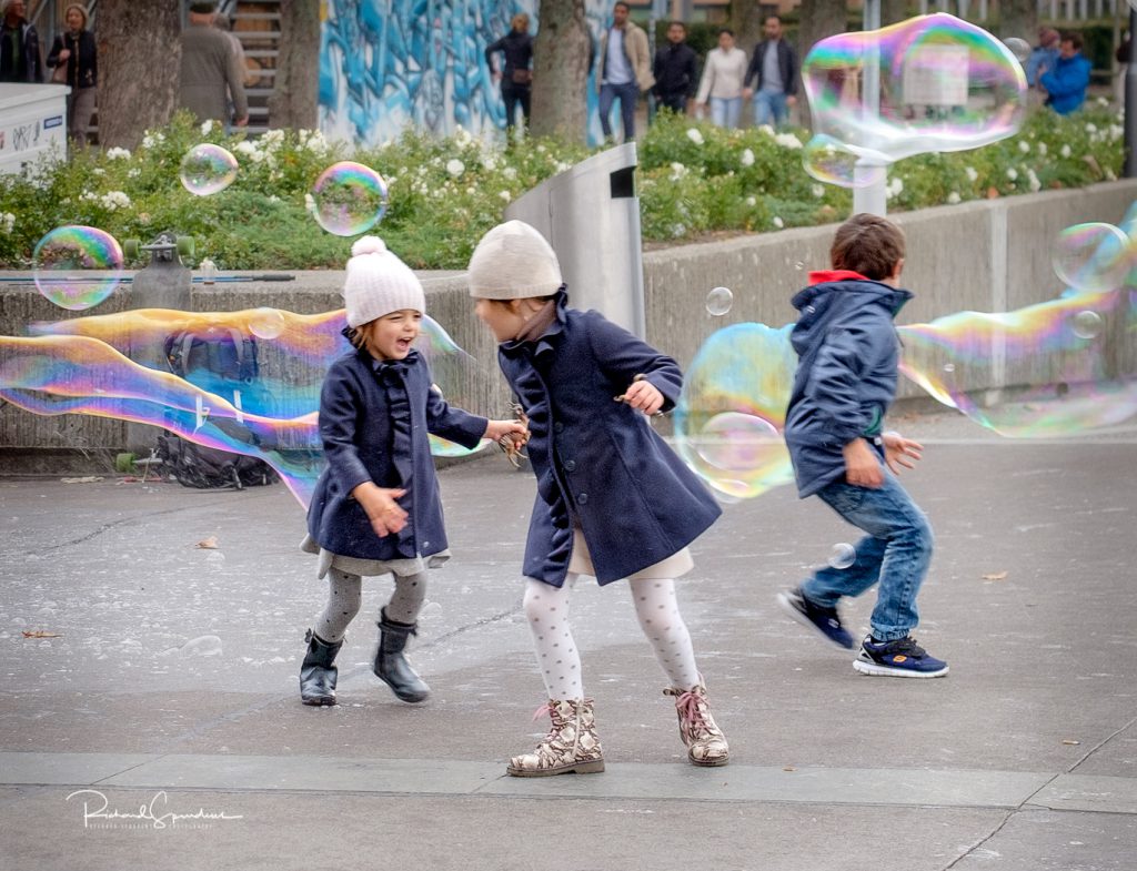 travel photography - travel photograher - images from a visit to zurich this featuring three children enjoying the fun of chasing large bubbles in a park