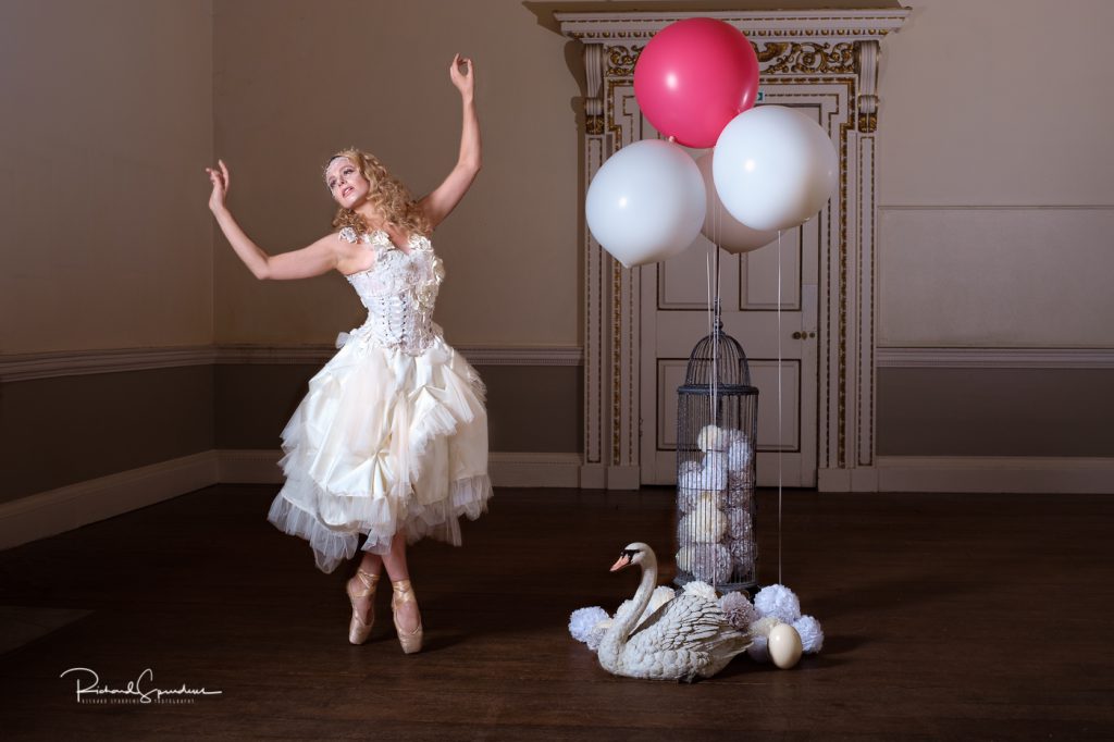 Dance Photographer - Dance photography - colour image showing dancer on pointe wearing a white corset dress and to her rhs is a swam with eggs and balllons so the image is called dancing at the swans party