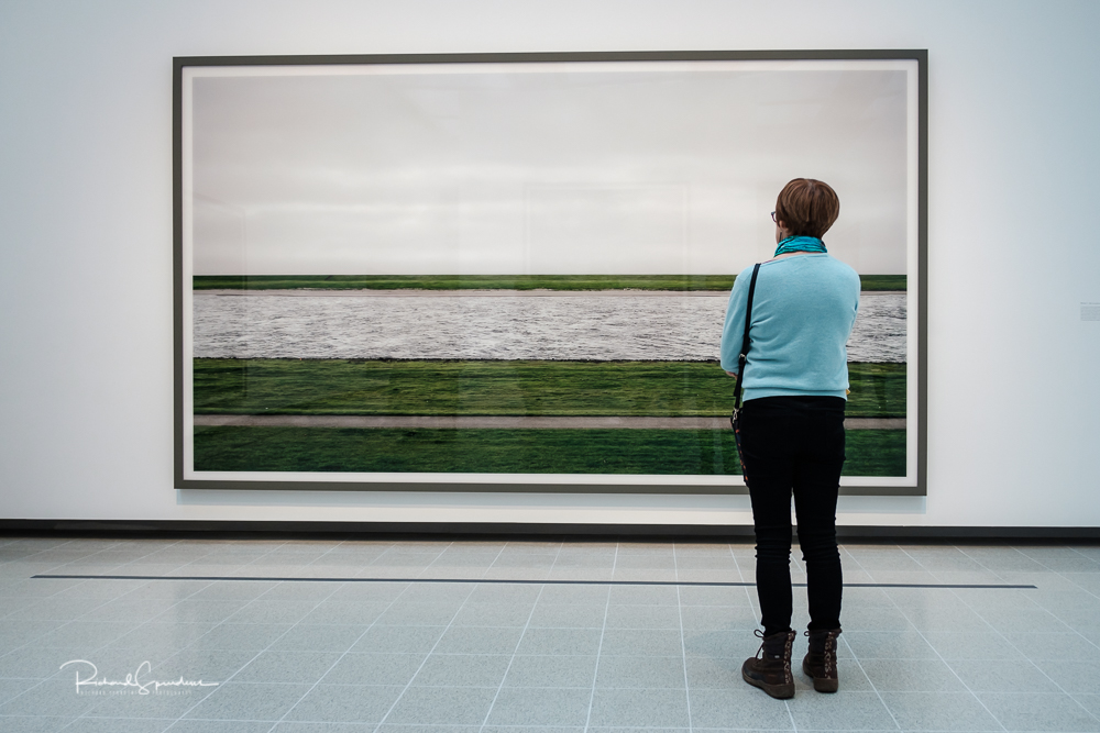 travel photography - travel photograher - colour image from a visit to the hayward gallery this visitor has a blue jumper with matches the wall colours she is viewing a large image of strips of green grass and then a large strip of water