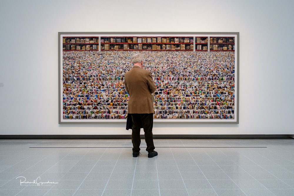 travel photography - travel photograher - colour image from a visit to the hayward gallery focusing on the visitors viewing the Gursky images, in this image a visitor wearing a brown jacket which seem to make the colours of image he is stood in front of