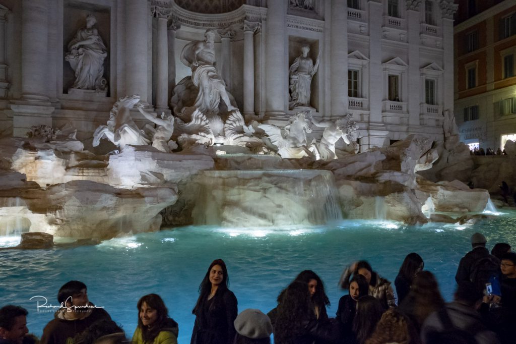 travel photography - travel photograher - colour image from a visit to rome this one from the trevi fountain square shot around 20:00 still lots of tourist and on lady is standing out as she poses for a picture in front of the great fountain.