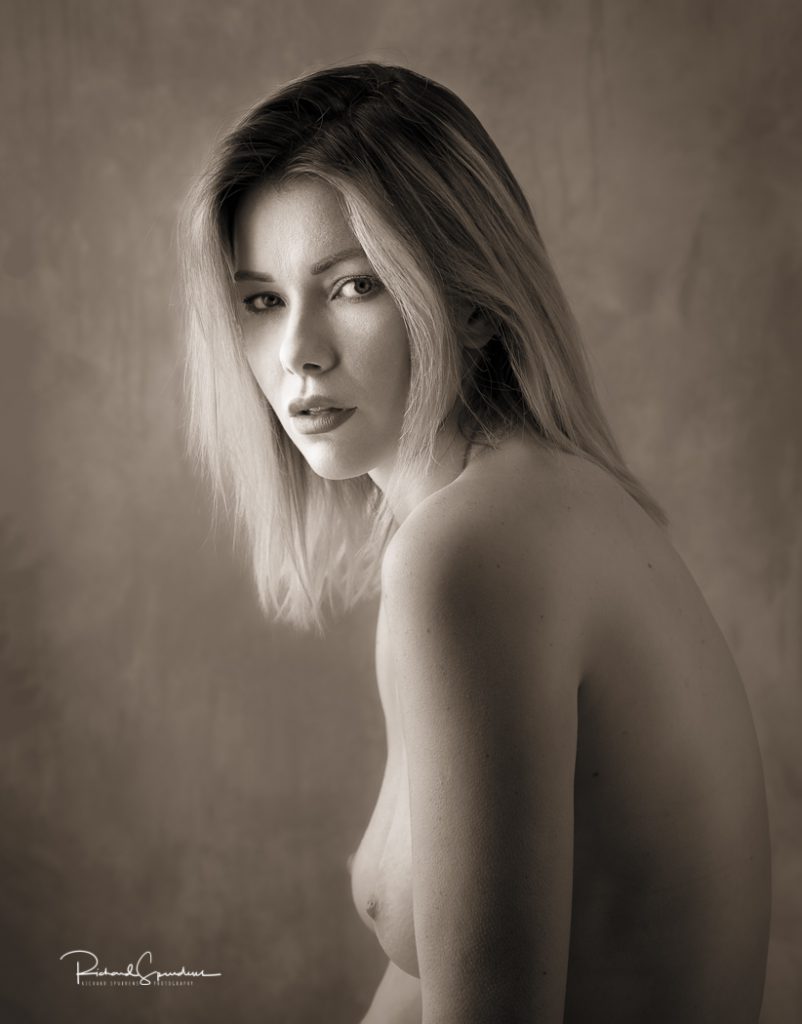 portrait photography - portrait photographer -a toned monochrome image head shot of the model nicky she is look across her shoulder and into the lens the lighting focused on her face and is producing some nice soft shadows