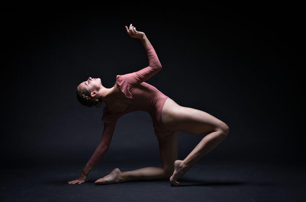 Dance Photographer - Dance photography - a colour image of dancer alya rose with bent legs and leaning back on her left arm with her right reaching up towards the light