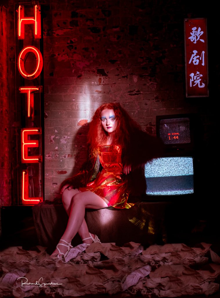 Fashion photographer - Fashion photography - colour image from electic dreams model wears a orange plastic skirt and red top and shor using neon lights - highlights 2019