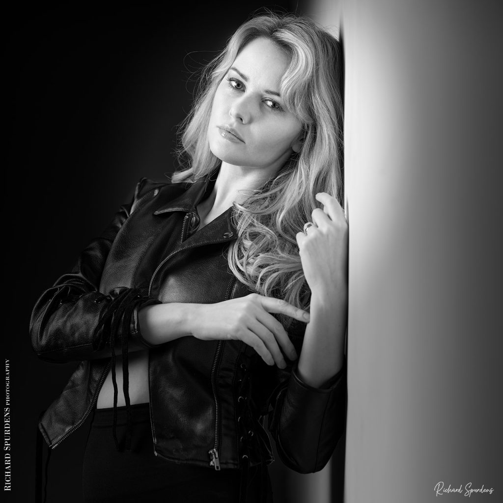 Fashion Photography - Fashion Photographer -model in her leather jacket leaning against the wall looking at the viewer