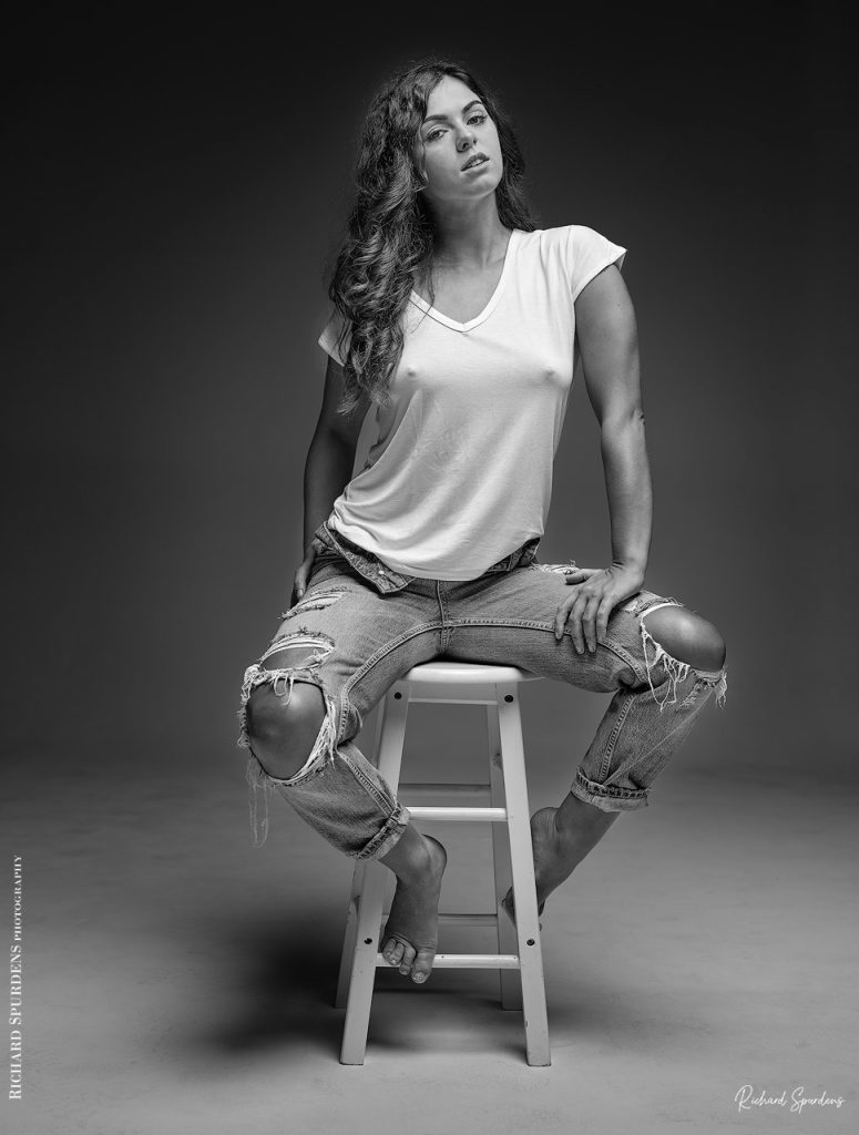 Fashion Photography - Fashion Photographer - model wearing torn jeans seated on a stool with a strong look towards the viewer