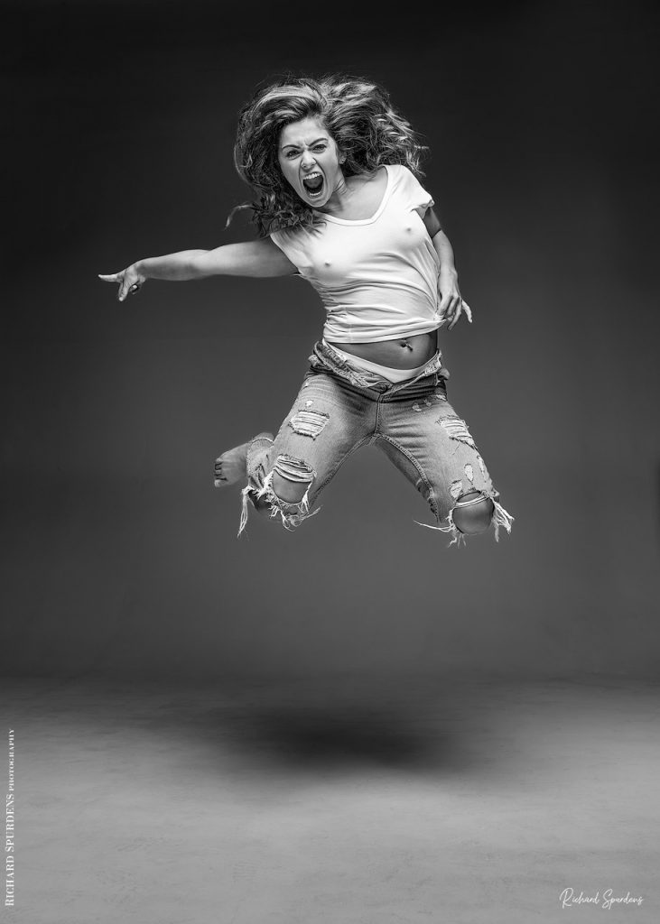 Fashion Photography - Fashion Photographer - model wearing torn jeans caught in mid air pointing out to the side of the her body