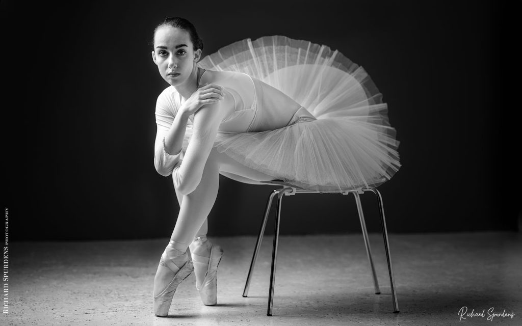 Dance Photographer - Dance photography - dancer erica wearing a white tute and seated on a chair holding her knees and looking towards the camera