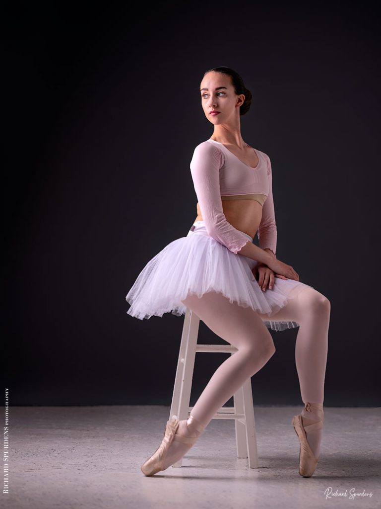 Dance Photographer - Dance photography - dancer Erica Mulkern seated on a stool wear a white tute and looking back to wards the light