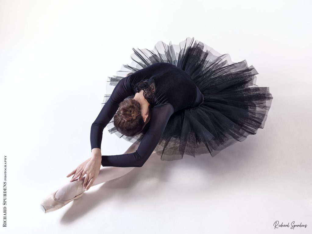 Dance Photographer - Dance photography - dancer Erica Mulkern wearing a black tutu as she stretches forward to a front foot. Shot from above to get the shape