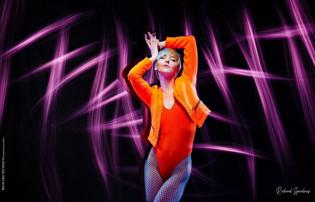 Light painting Photography - Fashion Photographer - colour image of model wearing orange jackets and body lighting swirls around the model using purple lights wands around the model